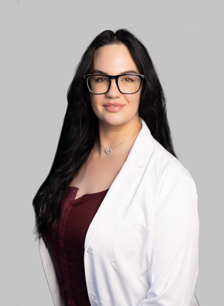 Female medical provider wearing a white lab coat, smiling, posed against a light gray background.